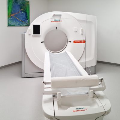 Raum mit einem CT-Gerät, ein blauer Kittel hängt rechts an der Wand